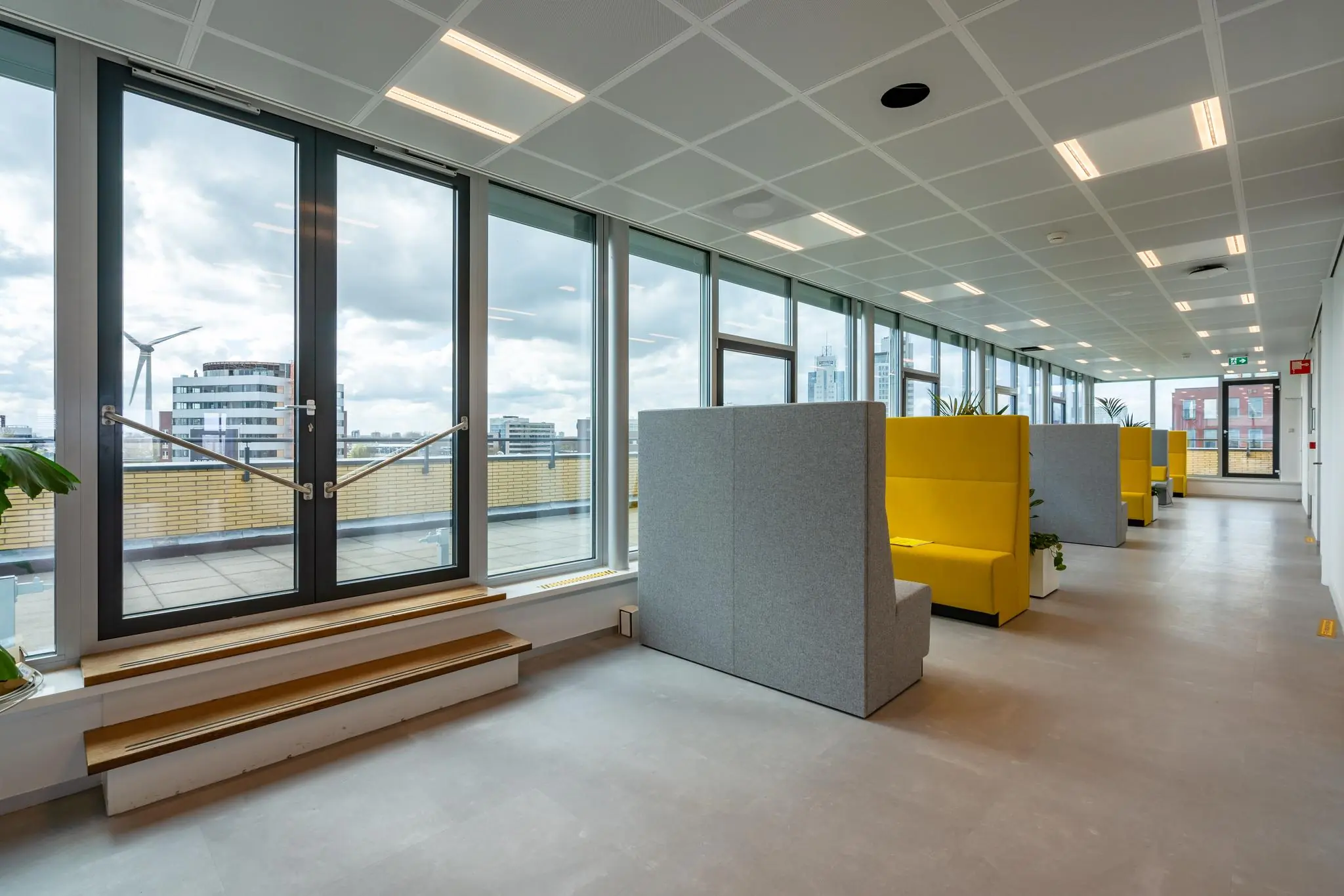 Moderne kantoorruimte aan de Fascinatio Boulevard met grote ramen, gele zitbanken en uitzicht op omliggende gebouwen.